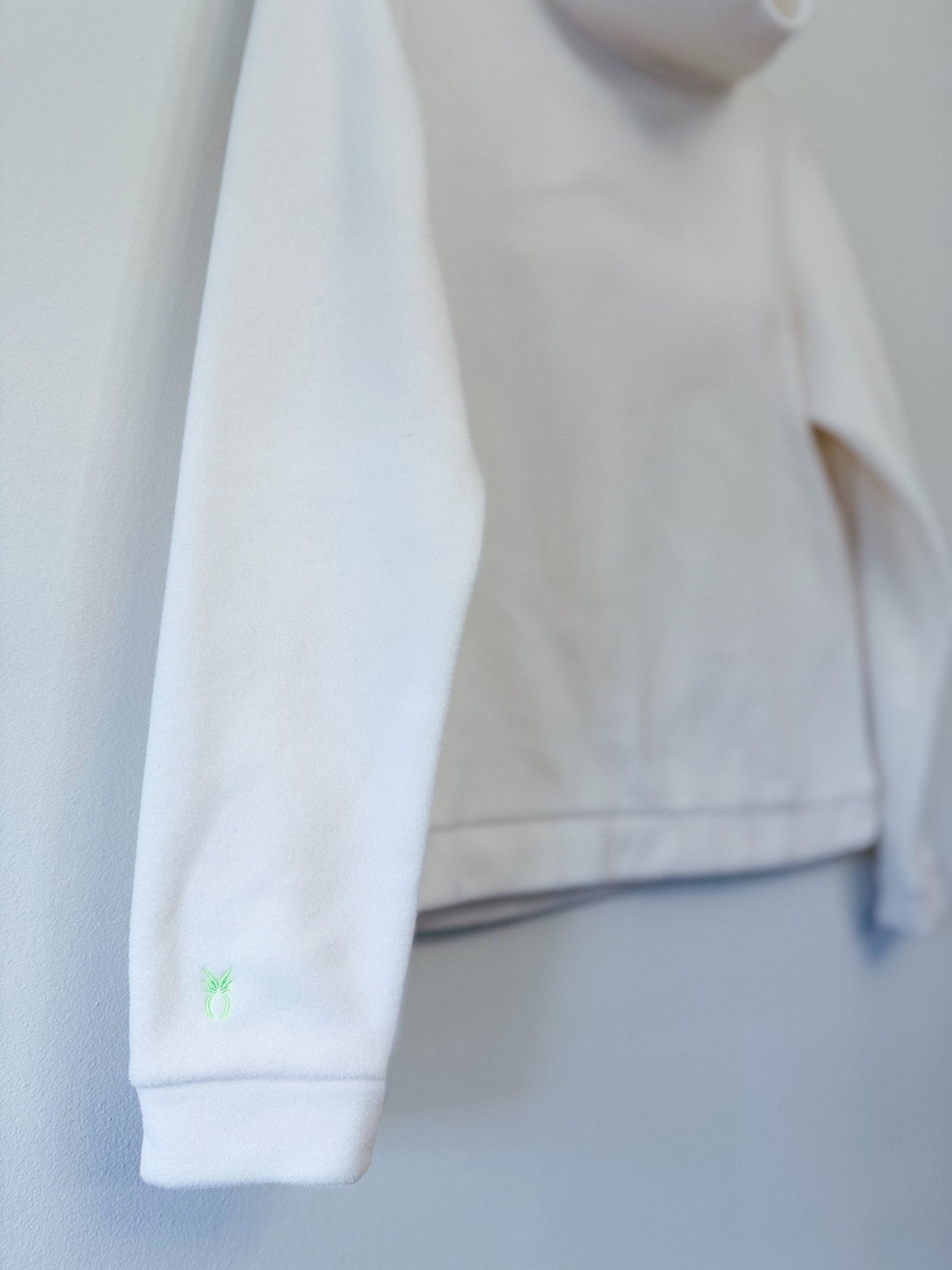 Close-up of a white sweatshirt with a green logo on a light gray background