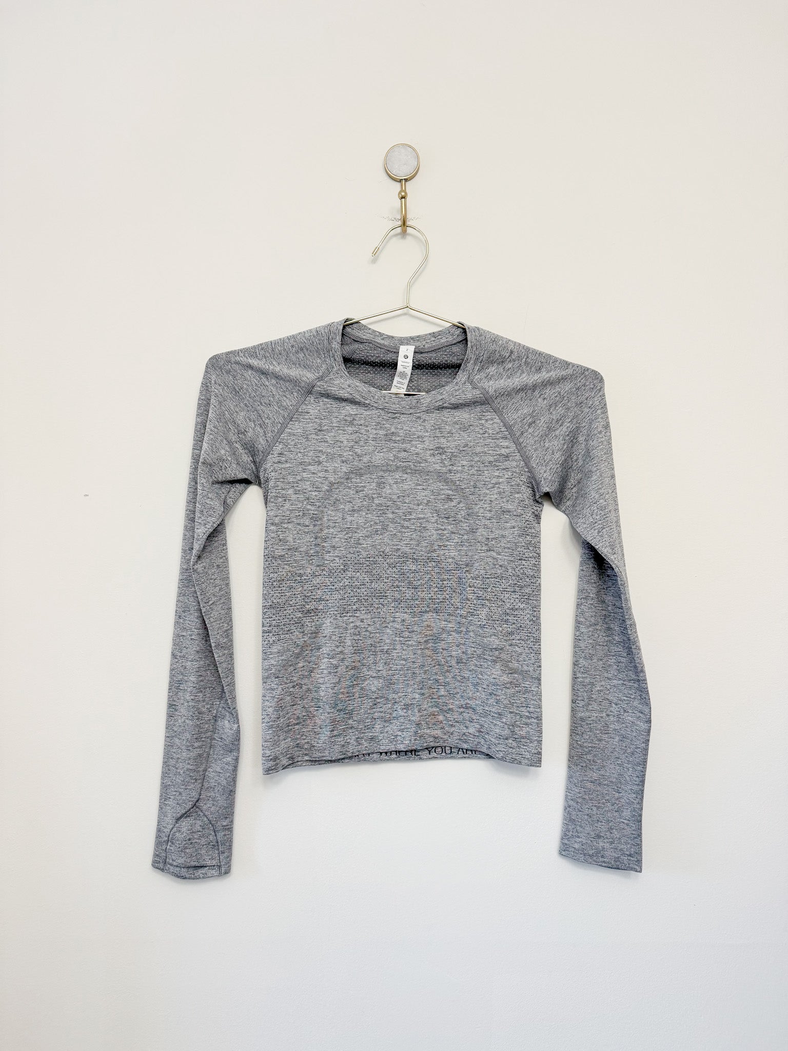 A white long-sleeve Lululemon Swiftly Tech shirt hanging on a hanger against a plain wall.