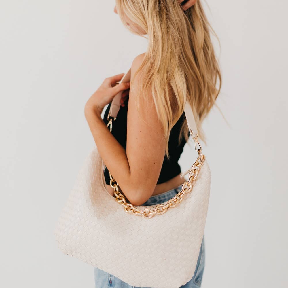 Person holding a white textured handbag with a gold chain strap against a light background