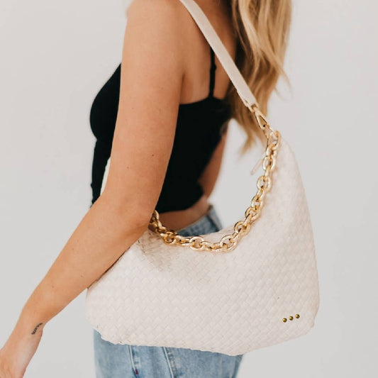 White handbag with gold chain strap held by a person against a neutral background