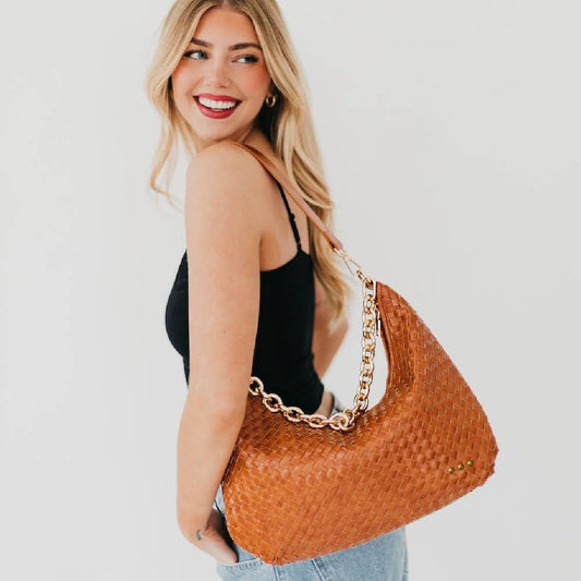 Woman holding a brown woven handbag with a gold chain strap on a plain background