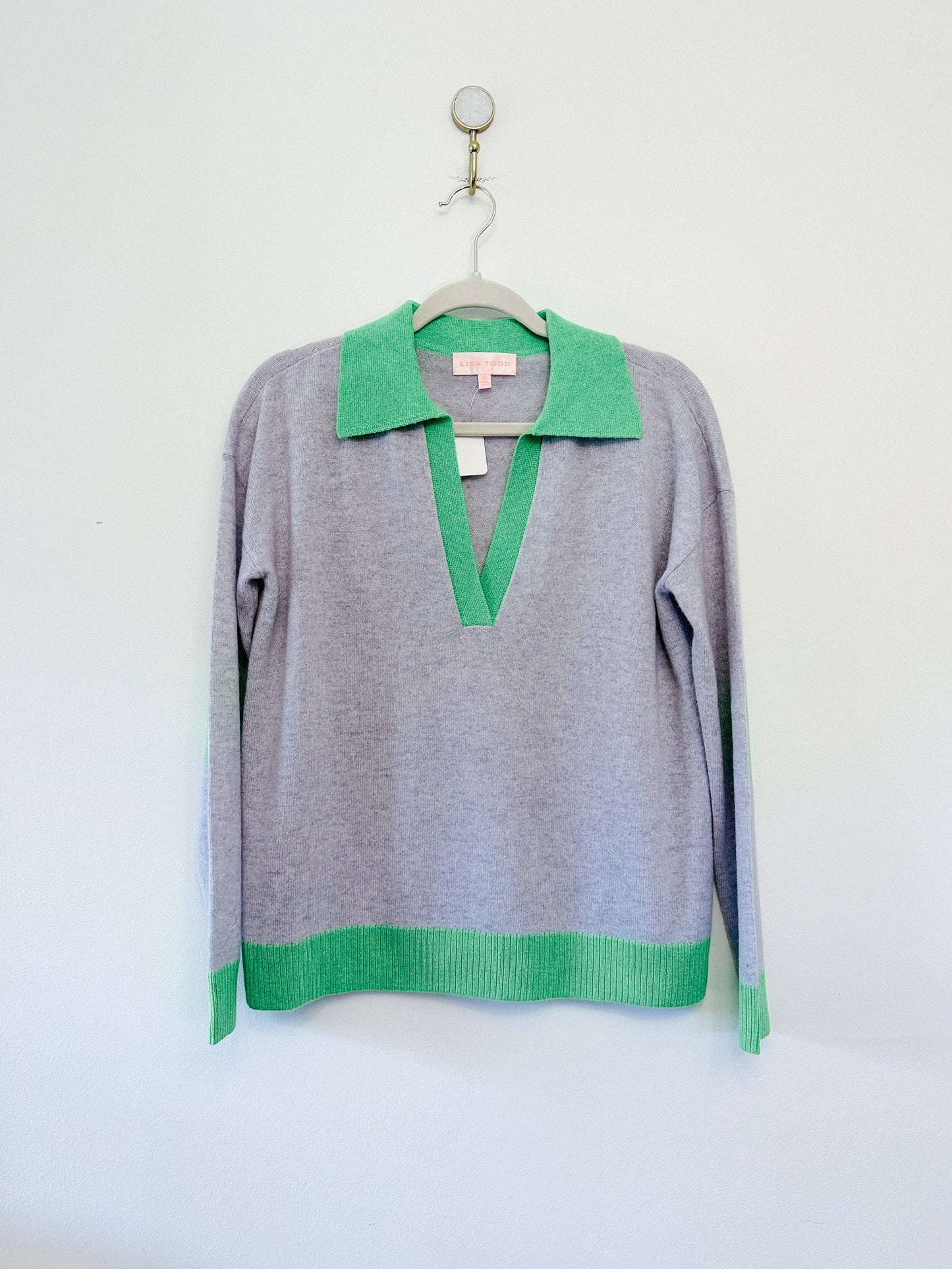 Gray sweater with green collar and cuffs on a hanger against a white background