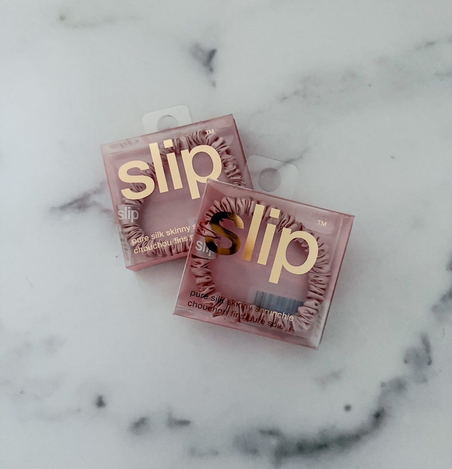 Two pink boxes of slip silk scrunchies on a marble surface