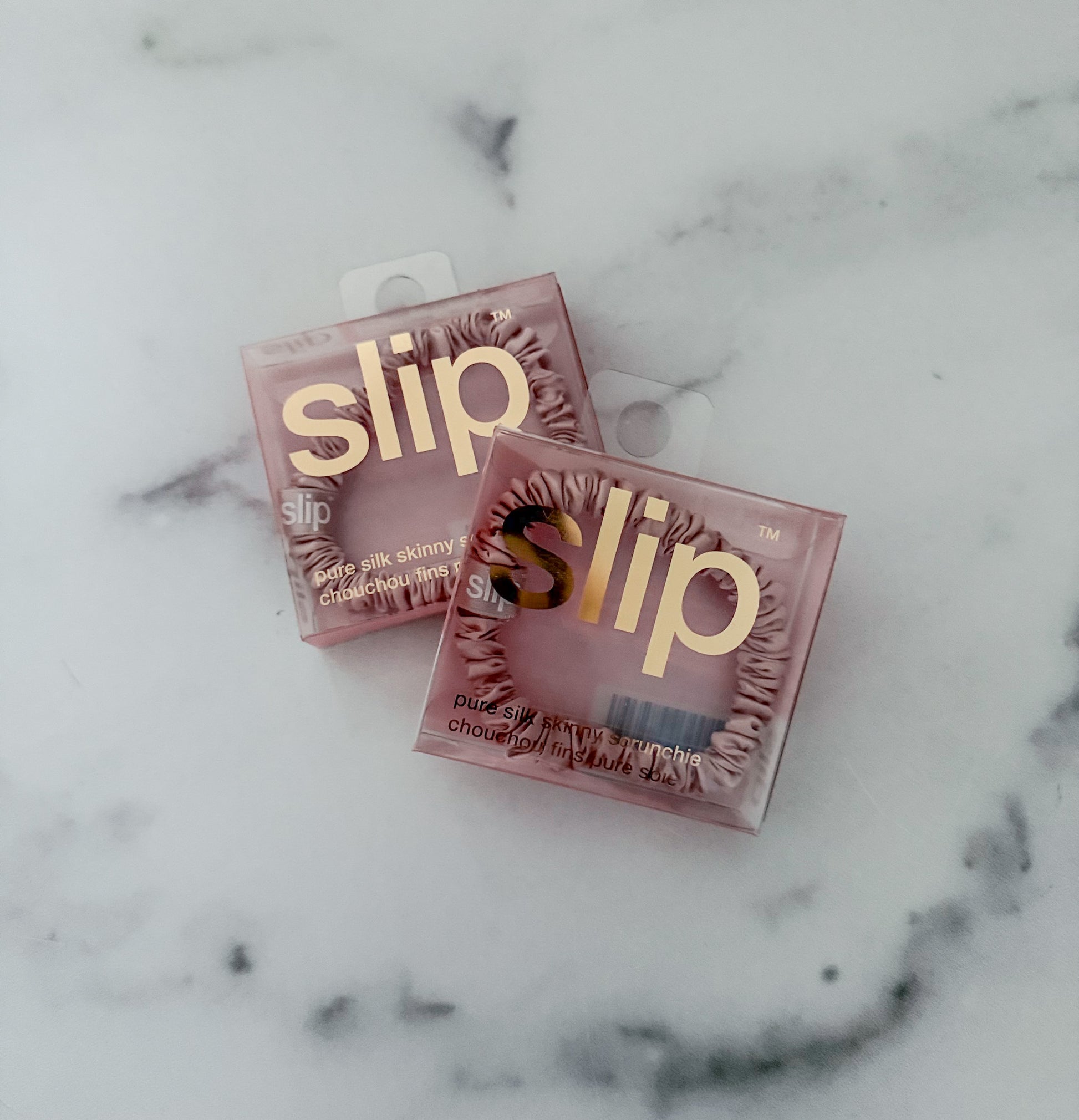 Two pink boxes of slip silk scrunchies on a marble surface