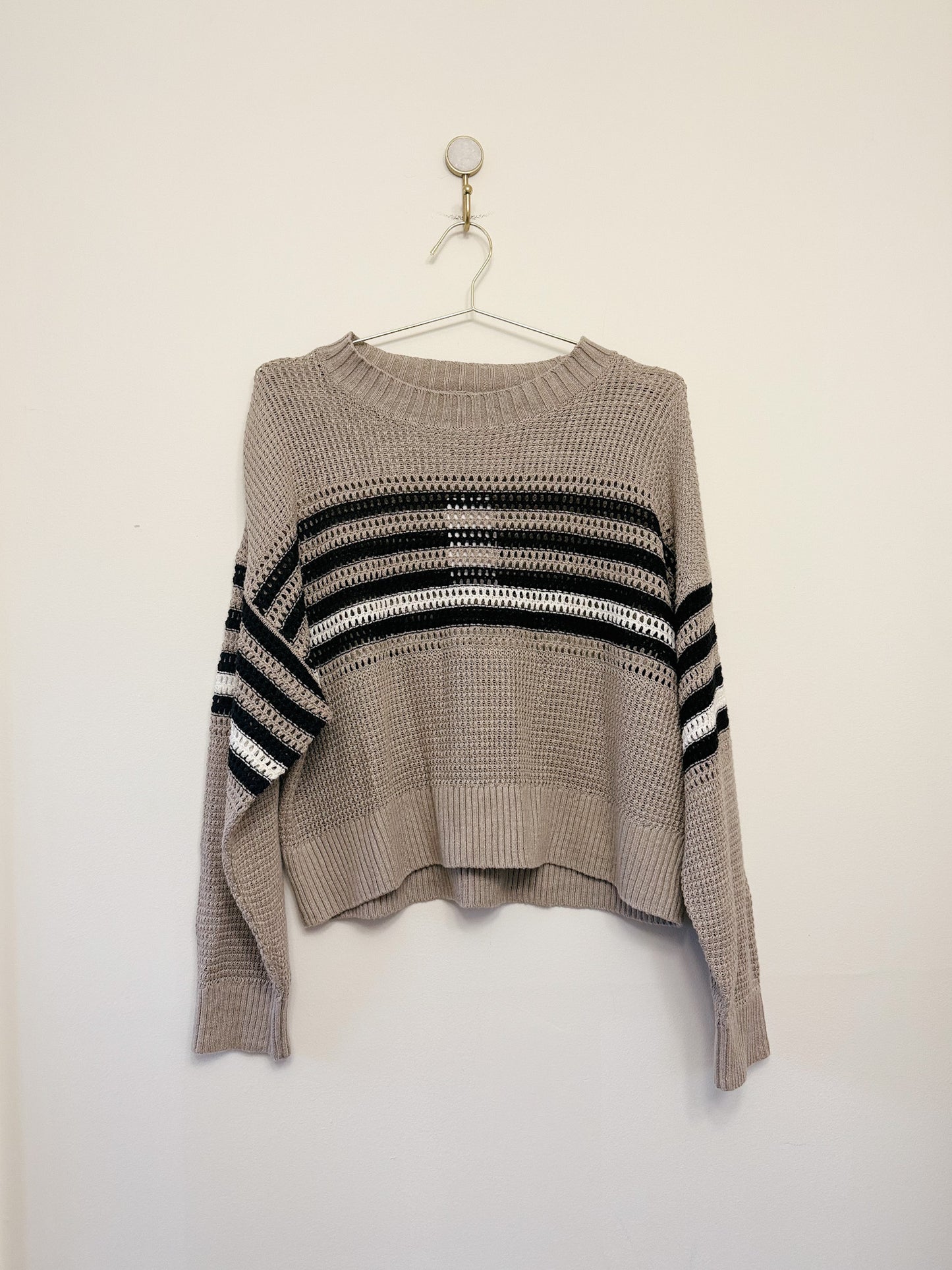 Beige sweater with black and white striped pattern on a hanger against a white background