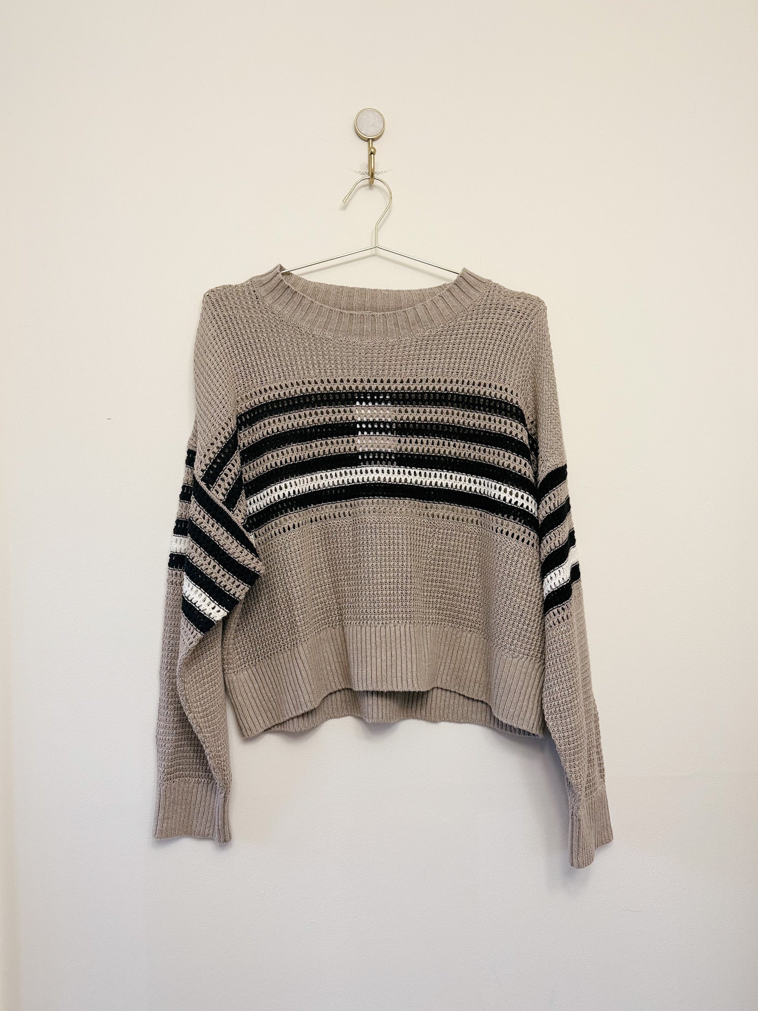 Beige sweater with black and white striped pattern on a hanger against a white background