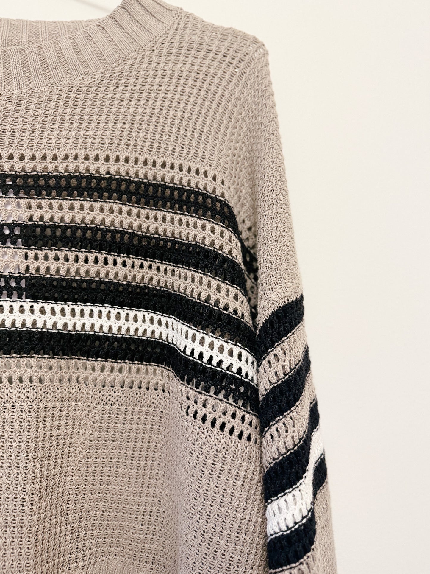 Close-up of a knitted sweater with black and white stripe pattern on a neutral background