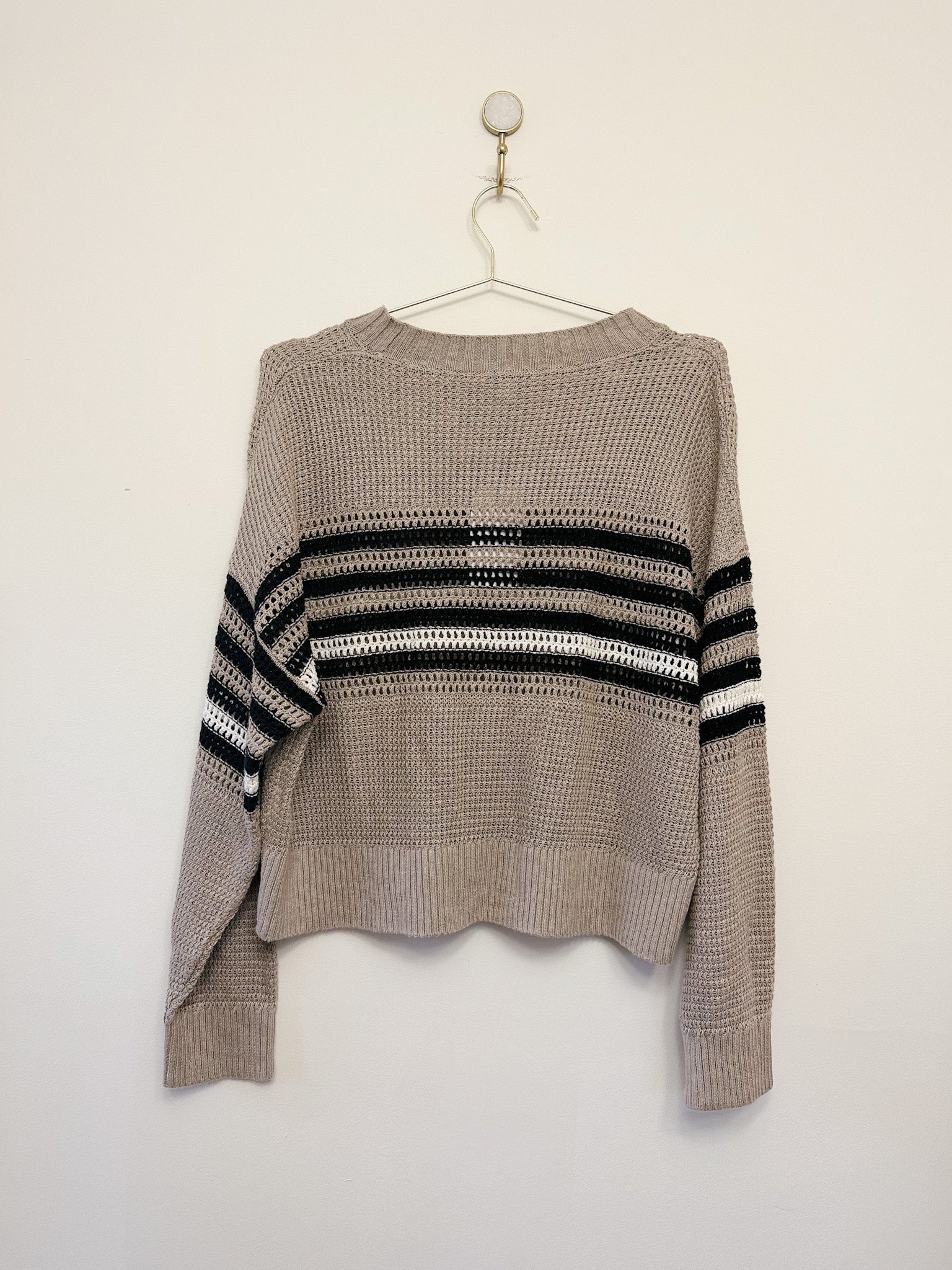 Beige sweater with black and white striped sleeves on a hanger against a white background