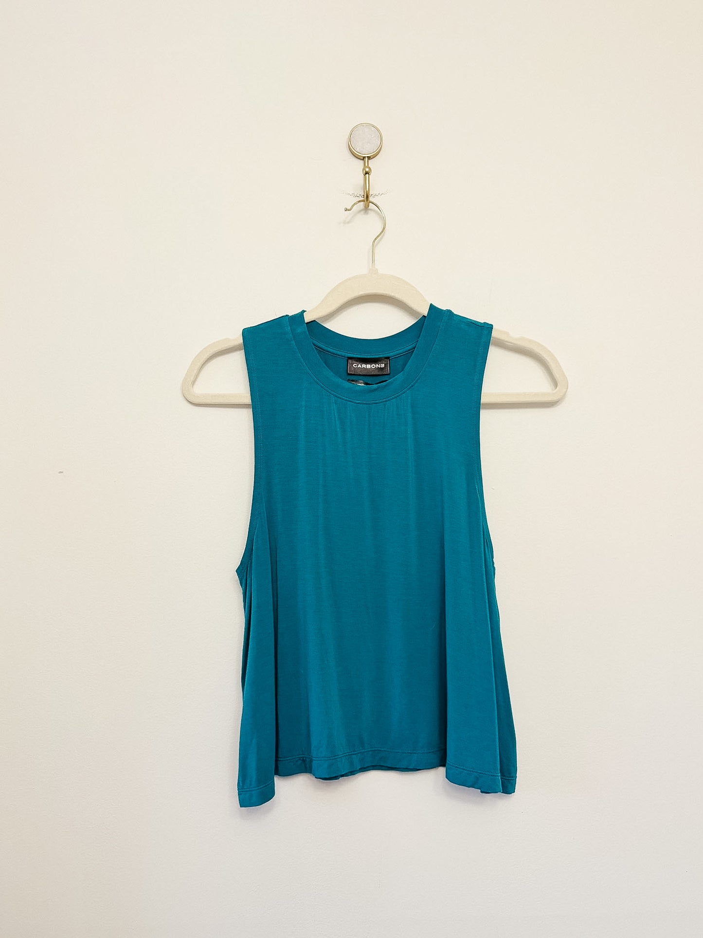 Carbon38 Crop Tank 2.0 teal sleeveless top on a hanger against a beige background