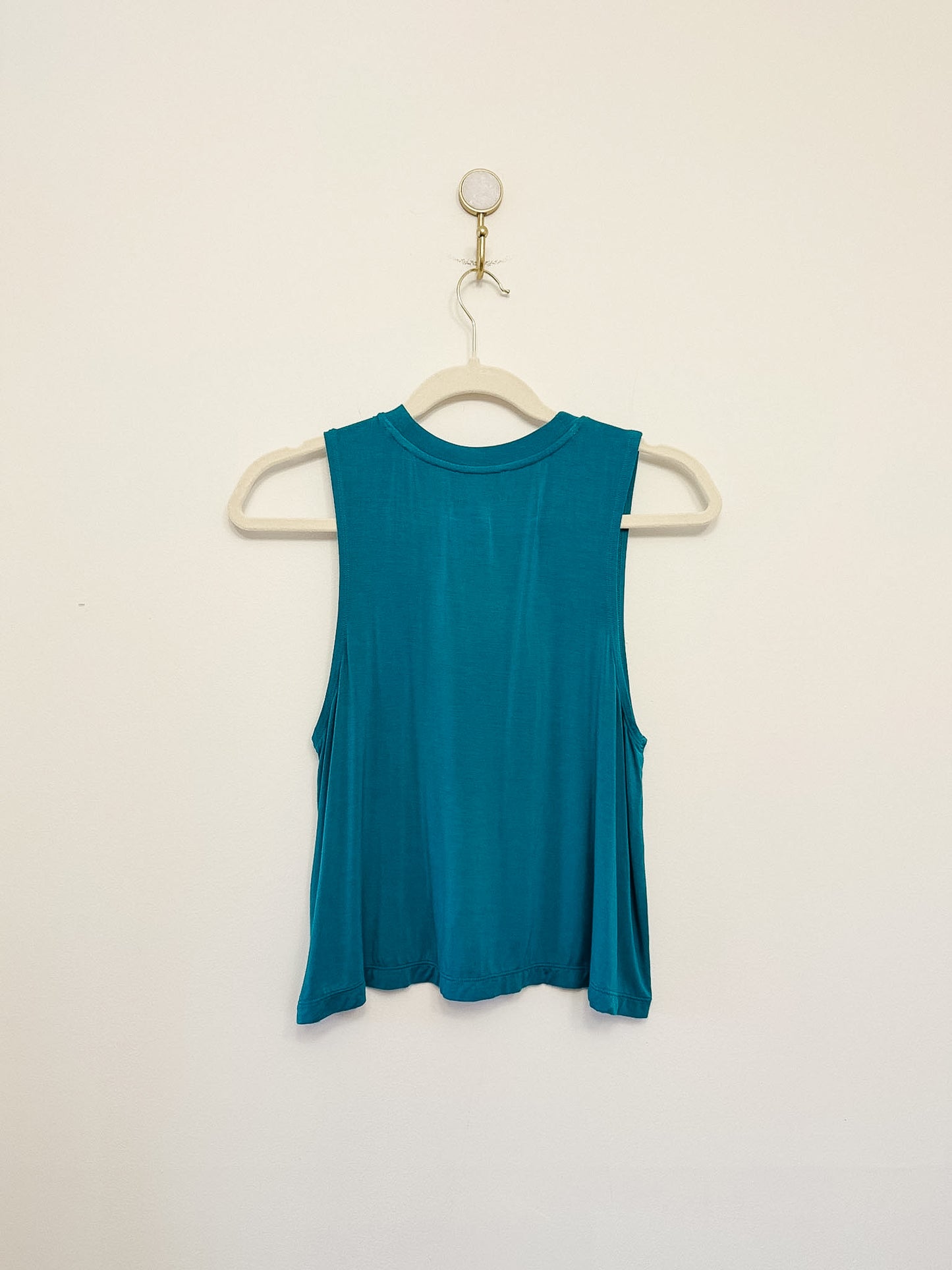 Carbon38 Crop Tank 2.0 teal sleeveless top on a hanger against a beige background