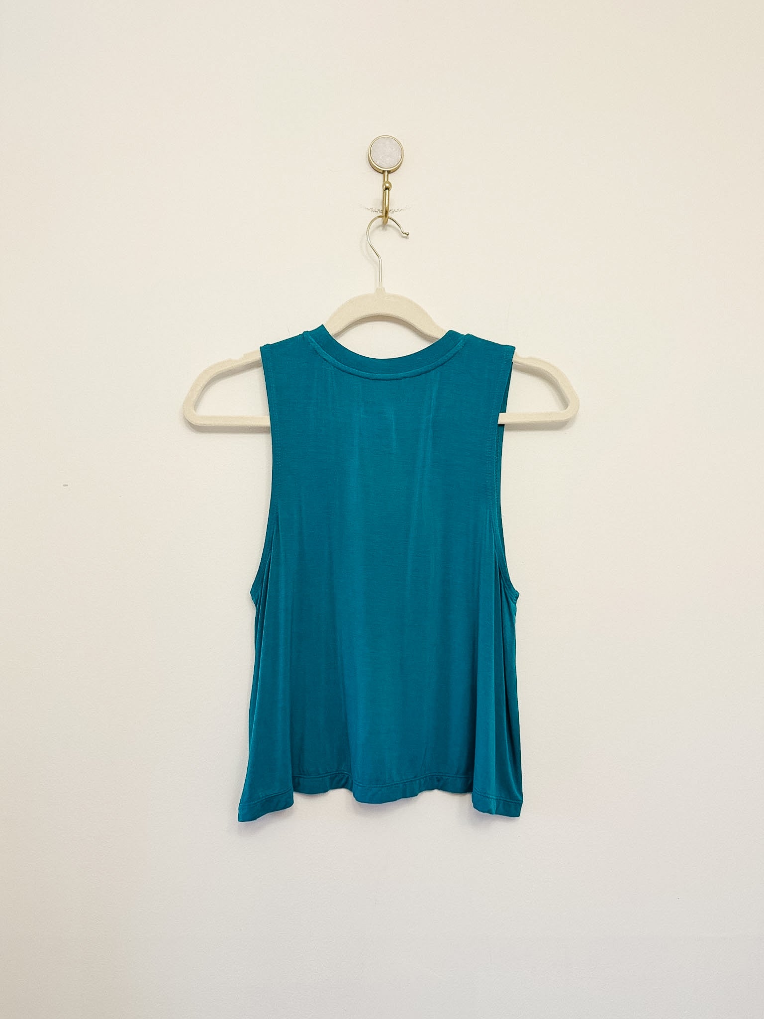 Carbon38 Crop Tank 2.0 teal sleeveless top on a hanger against a beige background