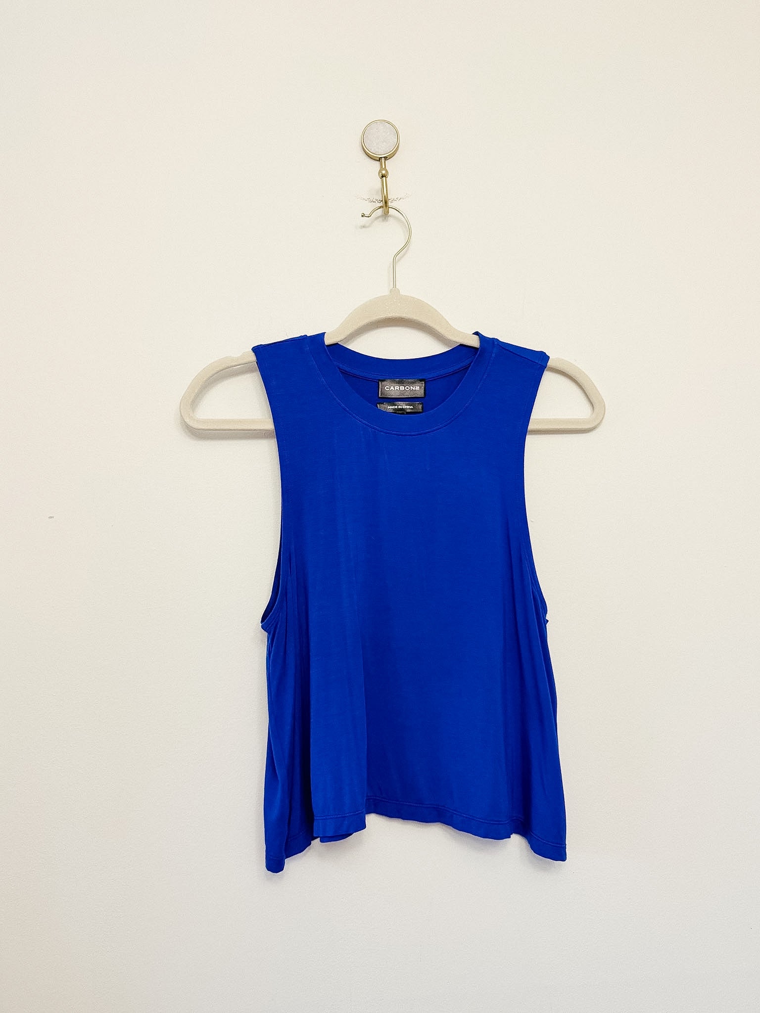 Carbon38 Crop Tank 2.0 blue sleeveless top on a hanger against a beige background