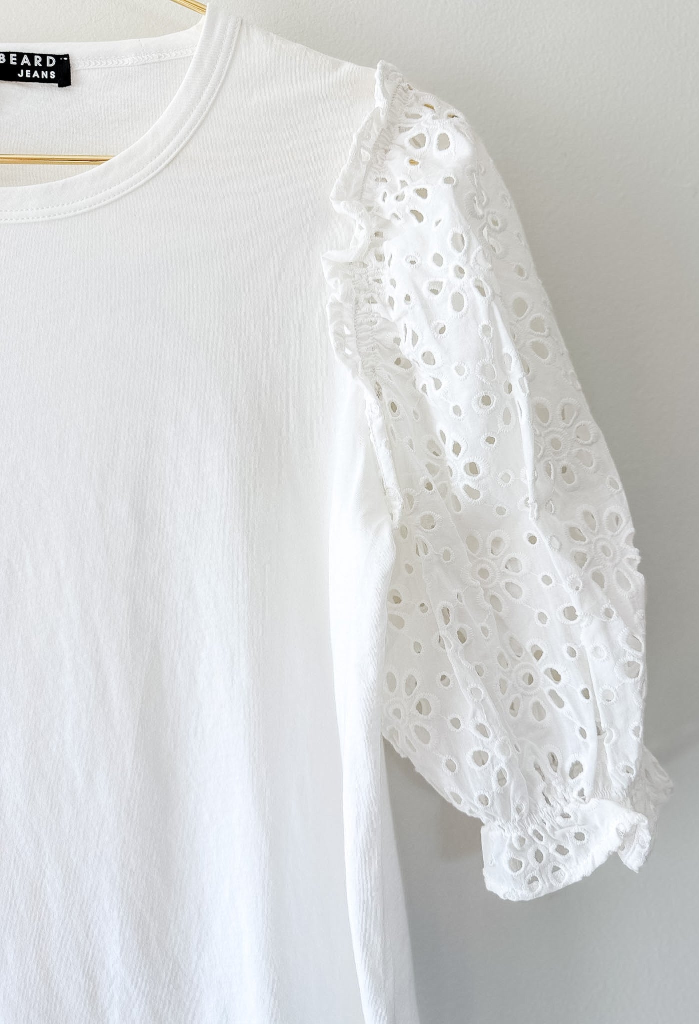 White blouse with eyelet sleeves on a hanger against a white background