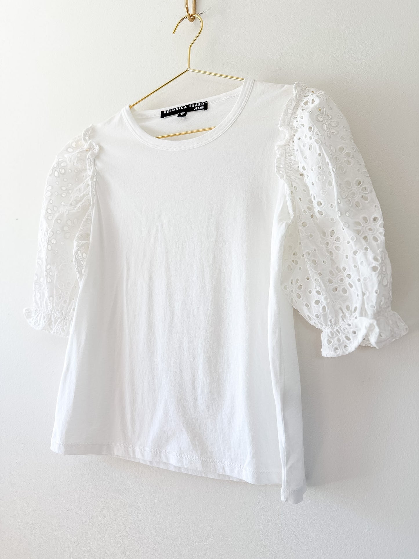 White blouse with eyelet sleeves on a hanger against a white background