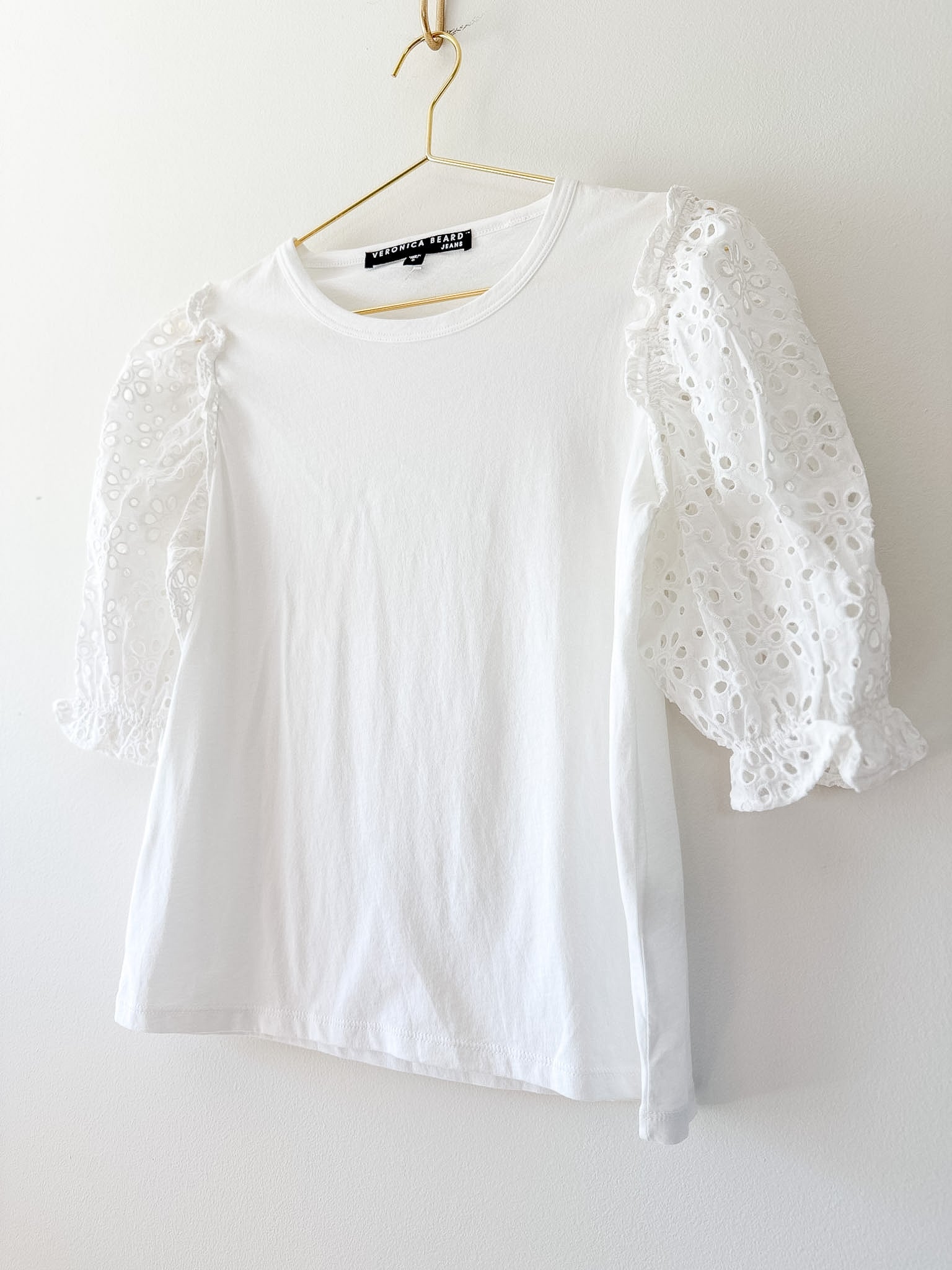 White blouse with eyelet sleeves on a hanger against a white background