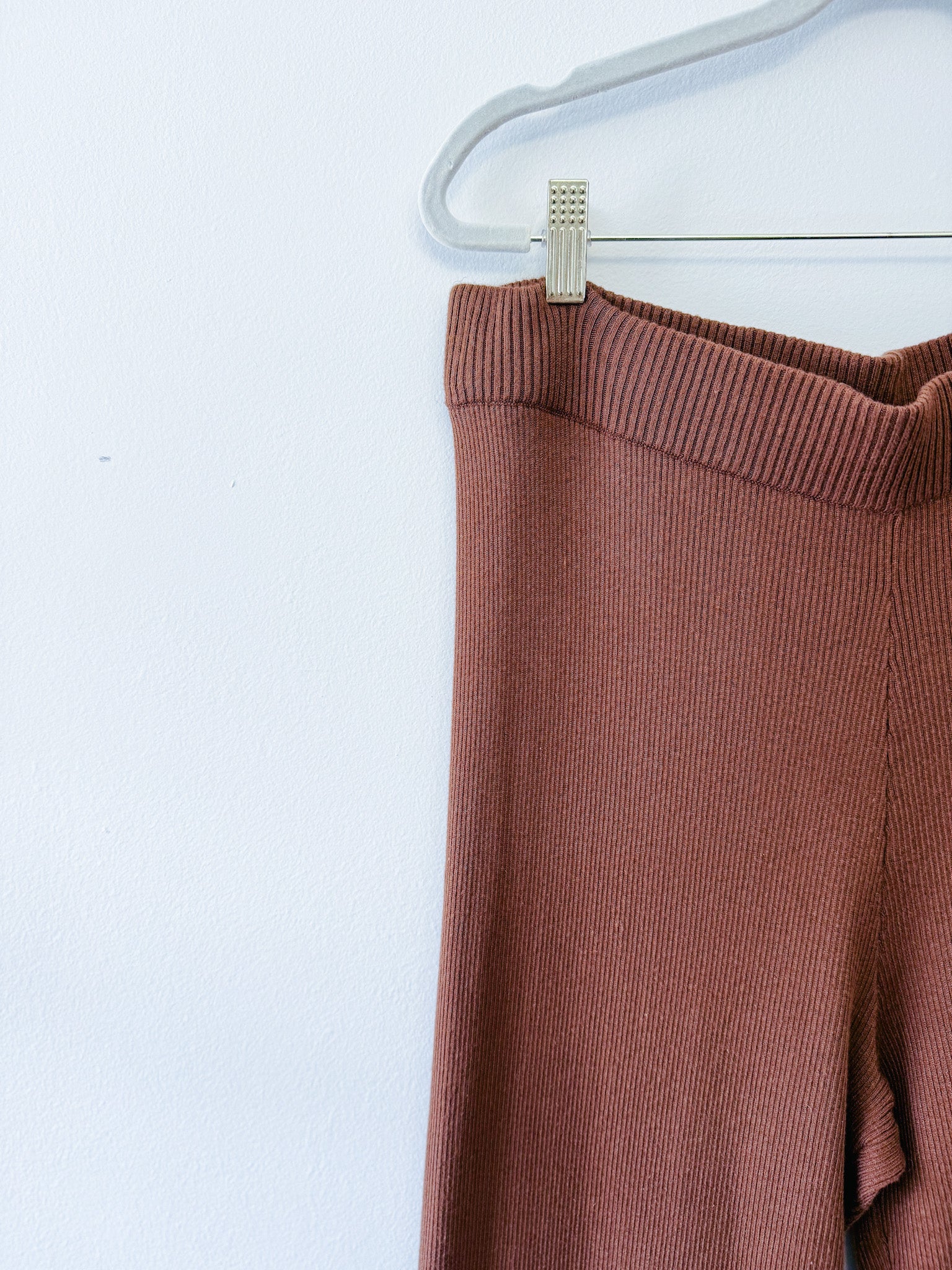 Brown ribbed knit pants on a hanger against a white background